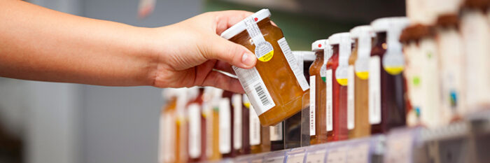 Hand grabs bottle of jam, glass bottles on supermarket shelf